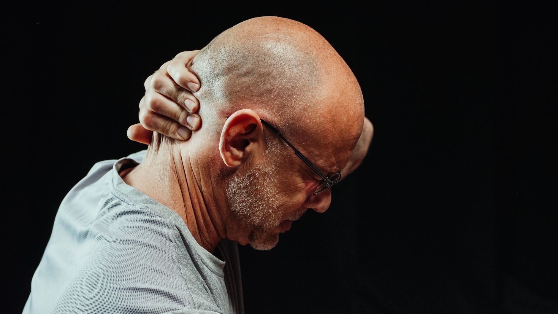 Bald man med glasögon håller handen mot nacken i smärta